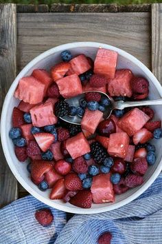 a white bowl filled with fruit on top of a wooden table next to blueberries and strawberries