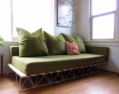 a green couch sitting on top of a hard wood floor next to a large window