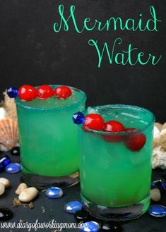 two glasses filled with green liquid and cherries on the rim, next to shells