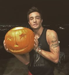 a man holding a carved pumpkin in front of his face with the city lights behind him