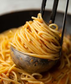 spaghetti being cooked in a skillet with tongs