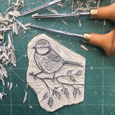 a bird on a branch is carved onto a piece of paper next to some wood shavings