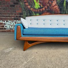 a blue and white couch sitting in front of a brick wall with graffiti on it