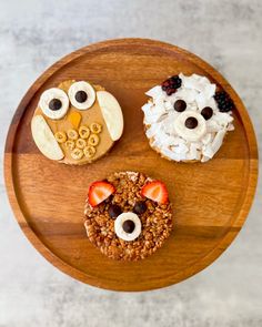 an overhead view of three desserts on a wooden platter with owl faces and fruit