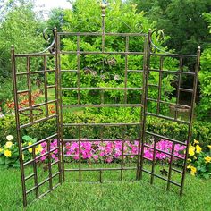 an iron garden trellis sitting in the middle of a flower bed filled with pink and yellow flowers