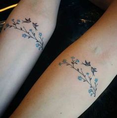 two people with matching tattoos on their arms, one has blue flowers and the other has green leaves