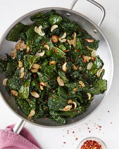 a pan filled with greens and nuts on top of a table