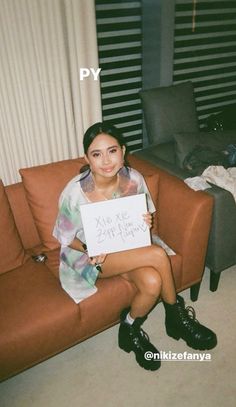 a woman sitting on top of a brown couch holding a sign