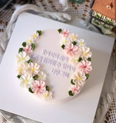 a white cake with pink and yellow flowers on it sitting on top of a table