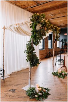 the wedding arch is decorated with greenery and white flowers, along with candles on the floor