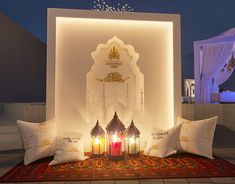 three lit candles sit on a rug in front of a wall with an arabic design