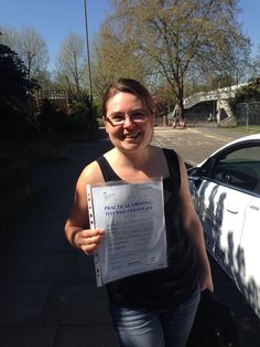 a woman standing next to a parked car holding up a paper with an award on it