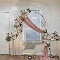 a white chair sitting in front of a pink and gold arch with flowers on it