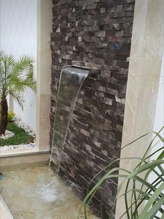 a water fountain in front of a brick wall and potted palm tree next to it