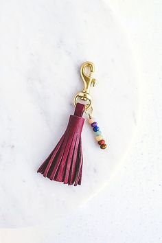 a red tasseled keychain on a white marble surface with a gold metal hook