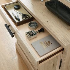 an open drawer on a wooden table with scissors and other items in it, including a notebook