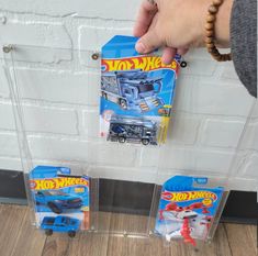 two toy trucks in plastic cases on a wooden floor next to a white brick wall