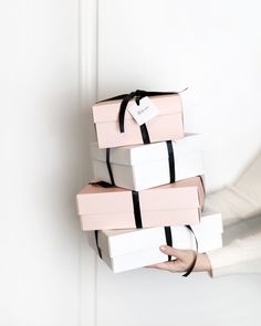 a stack of pink and white boxes with a black ribbon tied around the top, in front of a person's hand