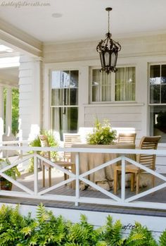 an outdoor dining table and chairs on a porch next to a white house with large windows