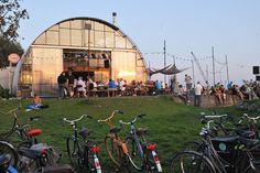 several bicycles parked in front of a building with people sitting at tables and hanging from the roof