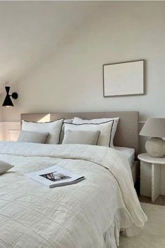 a white bed sitting under a window next to a table with a lamp on it