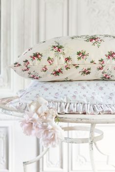 three pillows stacked on top of each other next to a white table with pink flowers