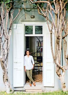 a woman standing in the doorway of a house surrounded by trees and bookshelves