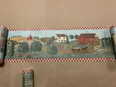 two rolls of toilet paper on the ground with farm scenes painted on one roll and red checkered border