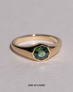 a gold ring with a green stone in the center on a white background that says, one of a kind