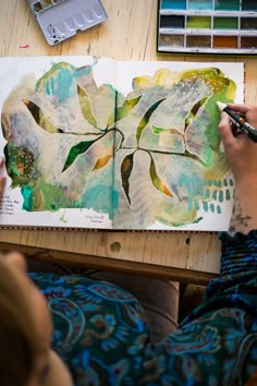 a person sitting at a table with an open book and paintbrushes in front of them