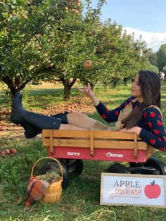 a woman is sitting in an apple orchard with her feet on the back of a wagon