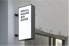 a small house big door sign mounted to the side of a white brick wall next to a window