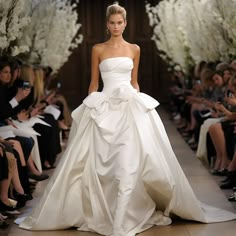 a woman in a white wedding dress walking down the runway