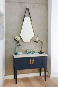 a blue table with a mirror and vase on it in front of a gray wall