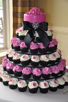 a triple tiered cake with pink and black cupcakes