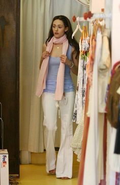 a woman walking through a clothing store with her pink scarf around her neck and white pants