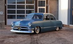 an old blue car parked in front of a building with a garage door and windows