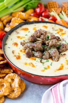 a bowl of dip with meatballs in it surrounded by crackers and veggies