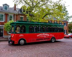 a red and green trolley is parked in front of a brick building on a cobblestone street