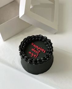 a black cake with red writing on it sitting in front of a white box that says vampire don't age