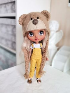 a doll with long blonde hair wearing overalls and a bear hat on top of a bed