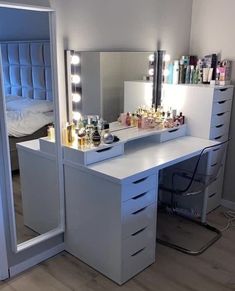 a white vanity with lighted drawers and mirror in a bedroom next to a bed that has its lights on