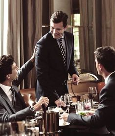 a man in a suit and tie standing over a table with other men at a restaurant