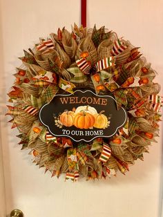 a welcome to our home wreath hanging on the front door with ribbon and pumpkins