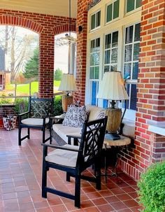 two chairs sitting on the front porch of a brick house with large windows and doors