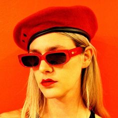 a woman wearing sunglasses and a red beret on top of her head in front of an orange wall