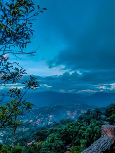 a view of the mountains and trees at dusk from atop a hill with clouds in the sky