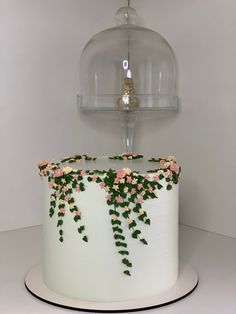 a white cake with pink and green flowers on the top is under a glass dome