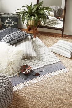 a living room filled with lots of pillows and blankets on top of a rug next to a mirror