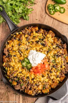 a skillet filled with mexican food on top of a wooden table next to green peppers and cilantro